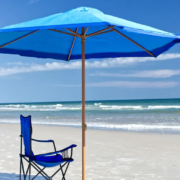 Blue beach umbrella with blue chair on beach with ocean waves