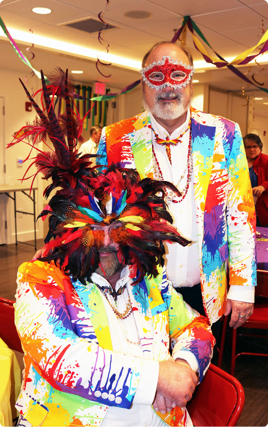 Male couple at Gilda's Club's Mardi Gras party dressed in bright, paint splattered suits wearing Mardi Gras masks